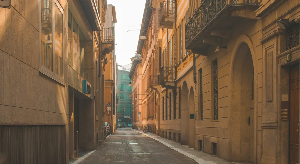 A quiet cobblestone alley lined with balconied buildings, sunlit at one end and lined with parked bicycles